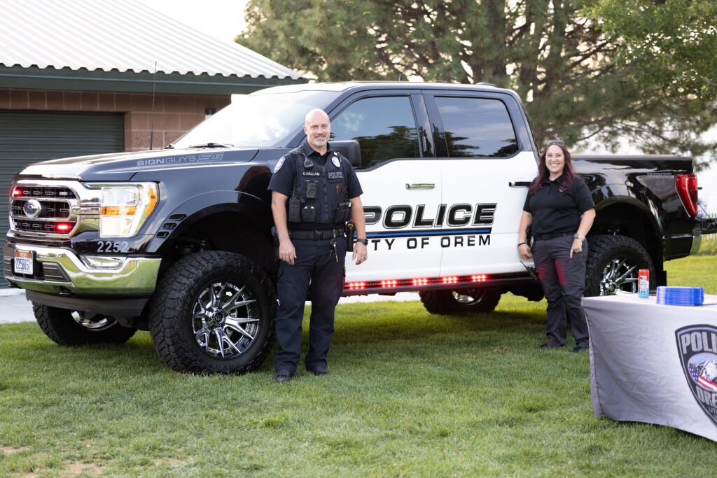 Picture of two officers standing in front of a police truck smiling in a community event