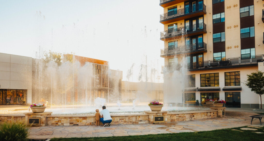 a father and son standing in front of a large water fountain at the shopping mall